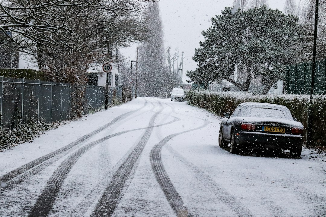 雪の積もった道路に停まる車。スタッドレスタイヤの使用限度を確認するイメージ